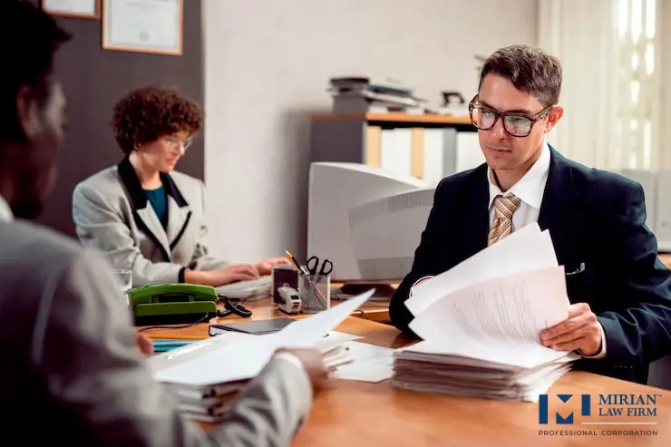 Two people are seated at an office desk piled with documents.