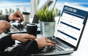 A close-up shot of two people working on a laptop displaying a digital "APPLICATION FORM", suggesting the online process of filing a WSIB claim.
