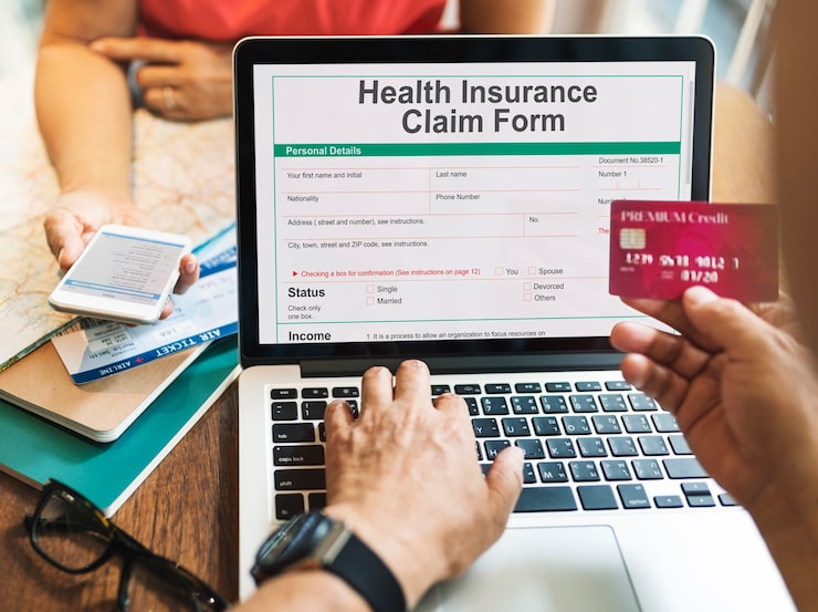 A close-up view of a person using a laptop to fill out a Health Insurance Claim Form, holding a credit card, emphasizing the administrative and financial steps in the personal injury claim process.