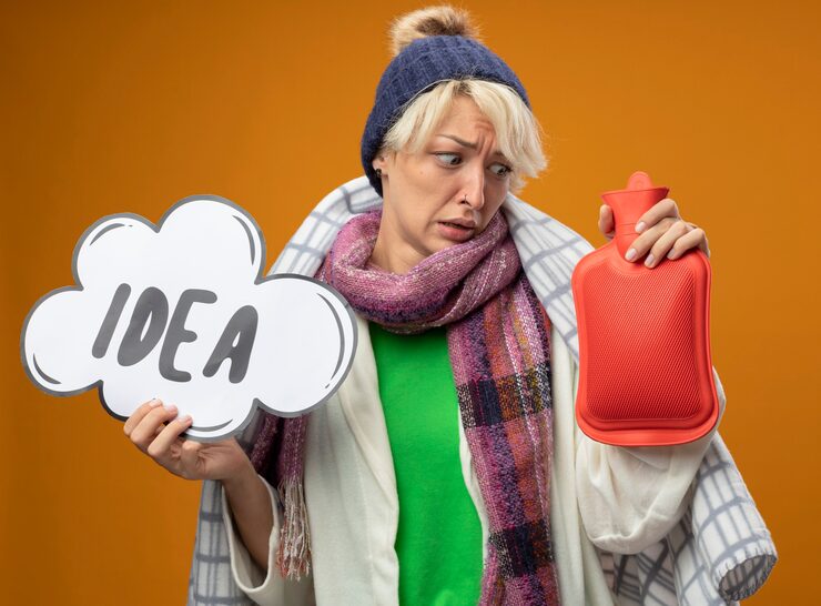 Woman in winter clothes looking worried, holding a red hot water bottle and a thought bubble with "IDEA."